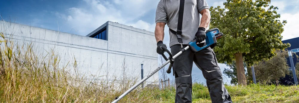 Person mäht hohes Gras mit Freischneider